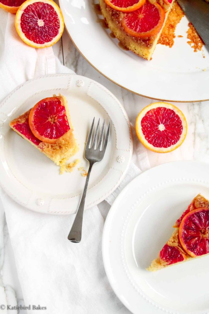 Two slices of upside down blood orange cake on white plates on a white marble surface