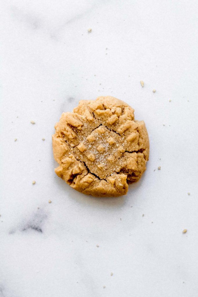 a single peanut butter cookie on a white surface with sugar sprinkled on top