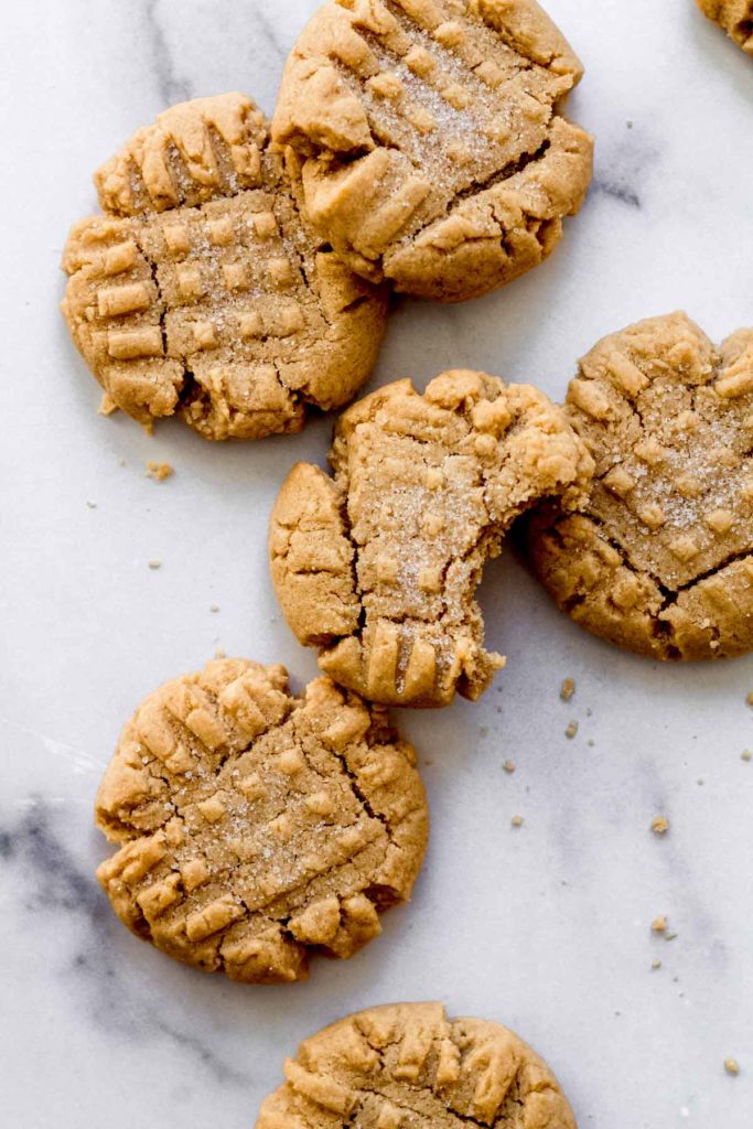 close up of a cookie with one bite taken out of it nestled among other cookies on a white surface