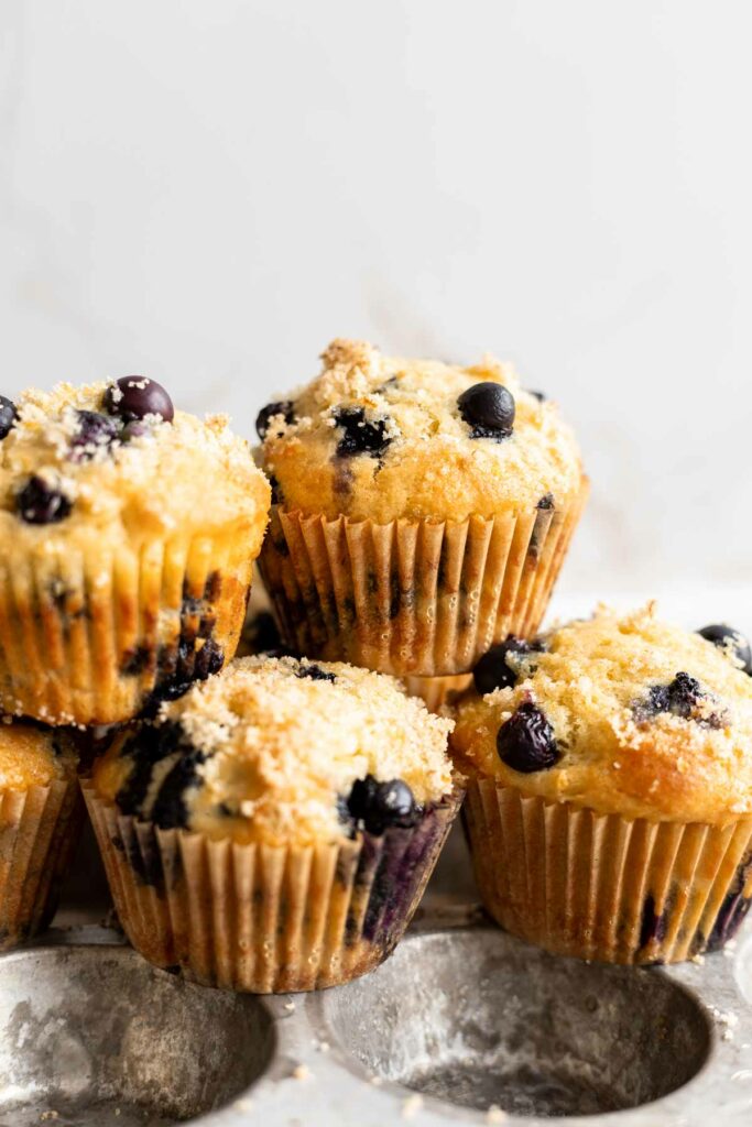 head-on view of several lemon blueberry muffins stacked on top of each other against a cream background