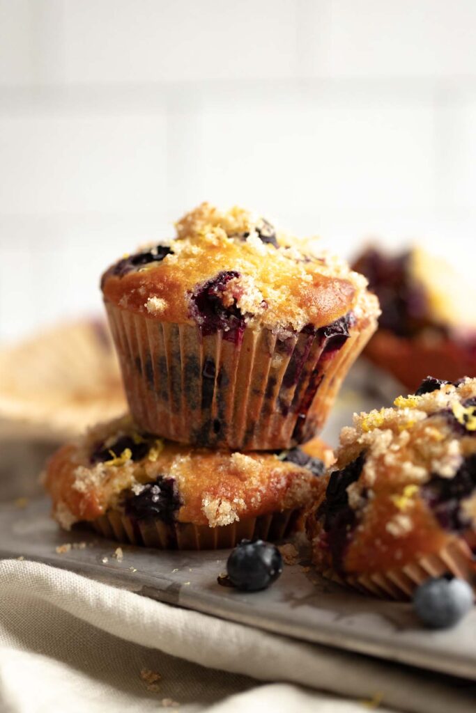 head-on view of lemon blueberry muffins stacked on top of each other in the muffin tin, against a cream background