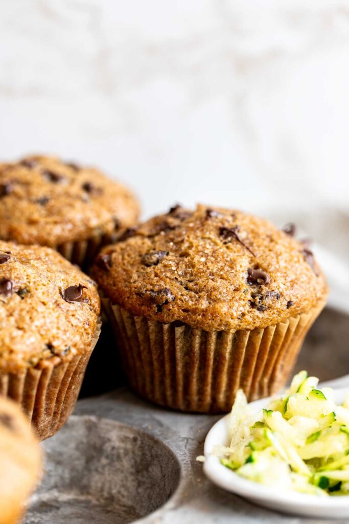 close up view of a finished zucchini chocolate chip muffin with grated zucchini on the side