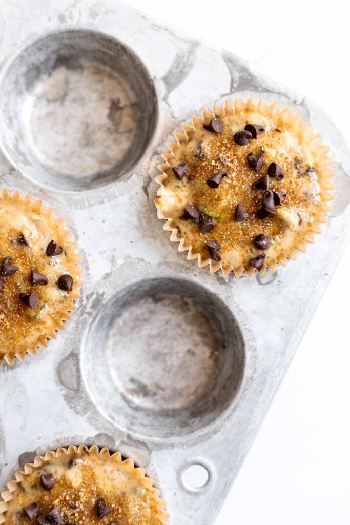 close up view of muffin batter in a muffin tin with mini chocolate chips on top, ready to go in the oven