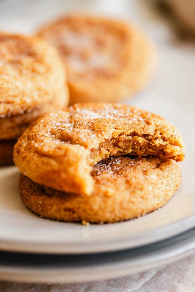 close up of a pumpkin snickerdoodle cookie on a plate with a bite taken out to expose the chewy texture