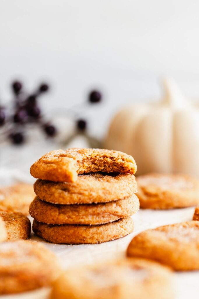 a vertical stack of finished snickerdoodles with a pumpkin in the background, the top cookie with a bite taken out of it